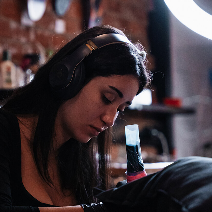 Female Melbourne tattoo artist, Elise Likidis tattooing client with headphones on
