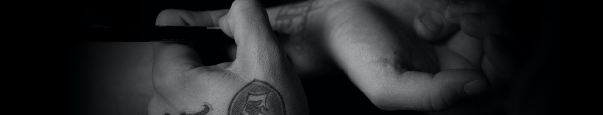 Person with tattooed hand holds an object in dramatic black-and-white lighting.