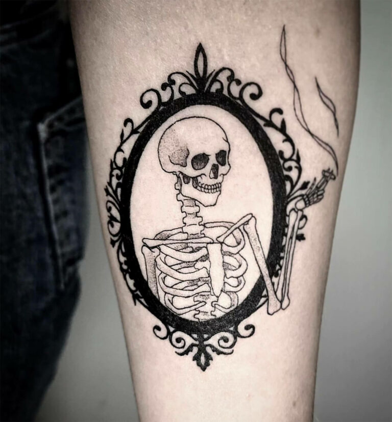 Black and grey tattoo of a skeleton smoking a cigarette in a decorative frame