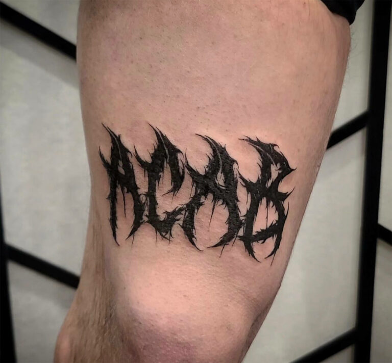Blackwork gothic script tattoo that reads 'ACAB' placed above the knee