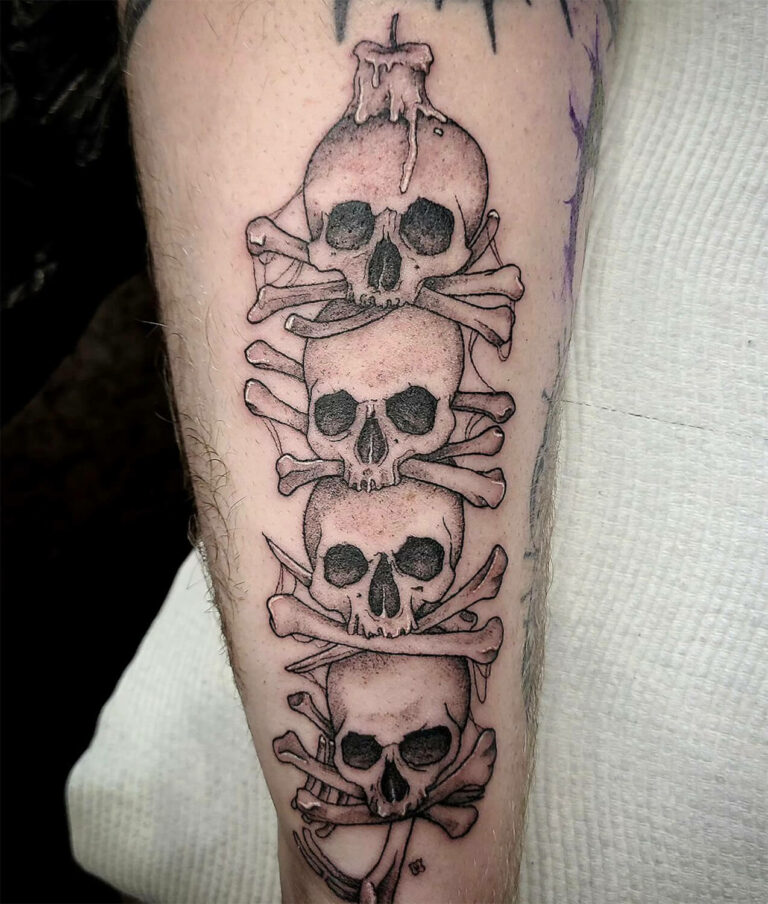 Black and grey tattoo of four skulls and crossbones stacked on top of each other on the client's forearm