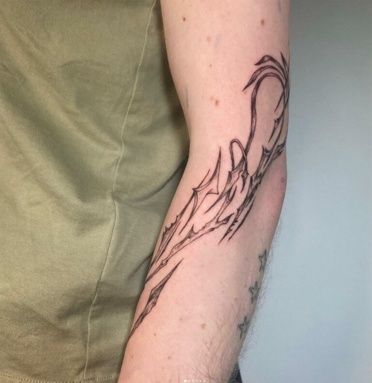 Person's forearm with black abstract line art and stars tattoo, wearing light green shirt.