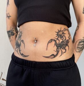 Symmetrical black/grey scorpion tattoos on either side of a woman's stomach