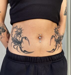 Symmetrical black/grey scorpion tattoos on either side of a woman's stomach