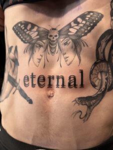 Surrealism script tattoo reading 'eternal' above the belly button