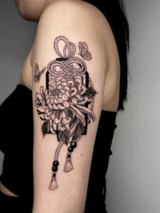 Blackwork and fineline omamori and chrysanthemum upper arm tattoo