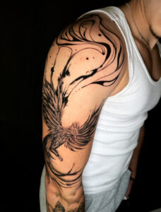 Black/grey phoenix tattoo on the bicep with abstract swirls extending up the shoulder