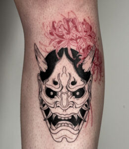 blackwork Hannya mask with red spider lilies tattooed on the shin