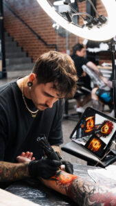 Male tattoo artist tattooing colorful design on forearm