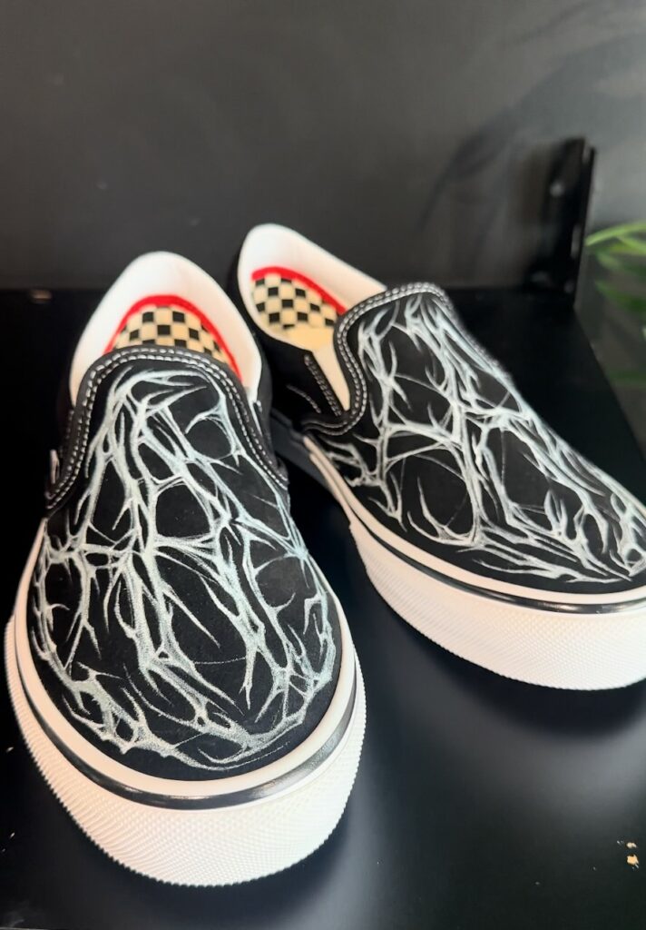 Black slip-on shoes with white branching pattern, checkerboard interior, and red accents.