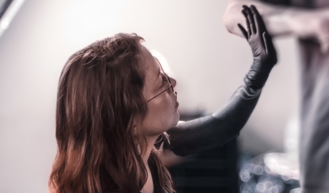 Person with glasses intently examines a forearm wearing a black glove.