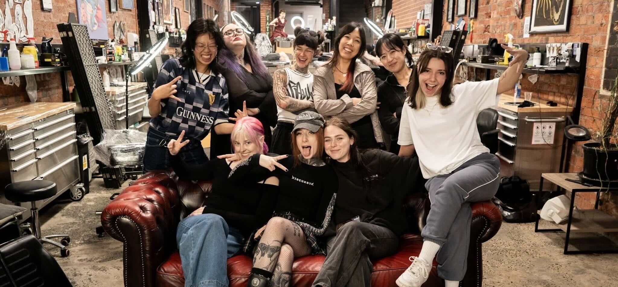 Nine people posing in a creative studio around a red leather couch with brick walls.