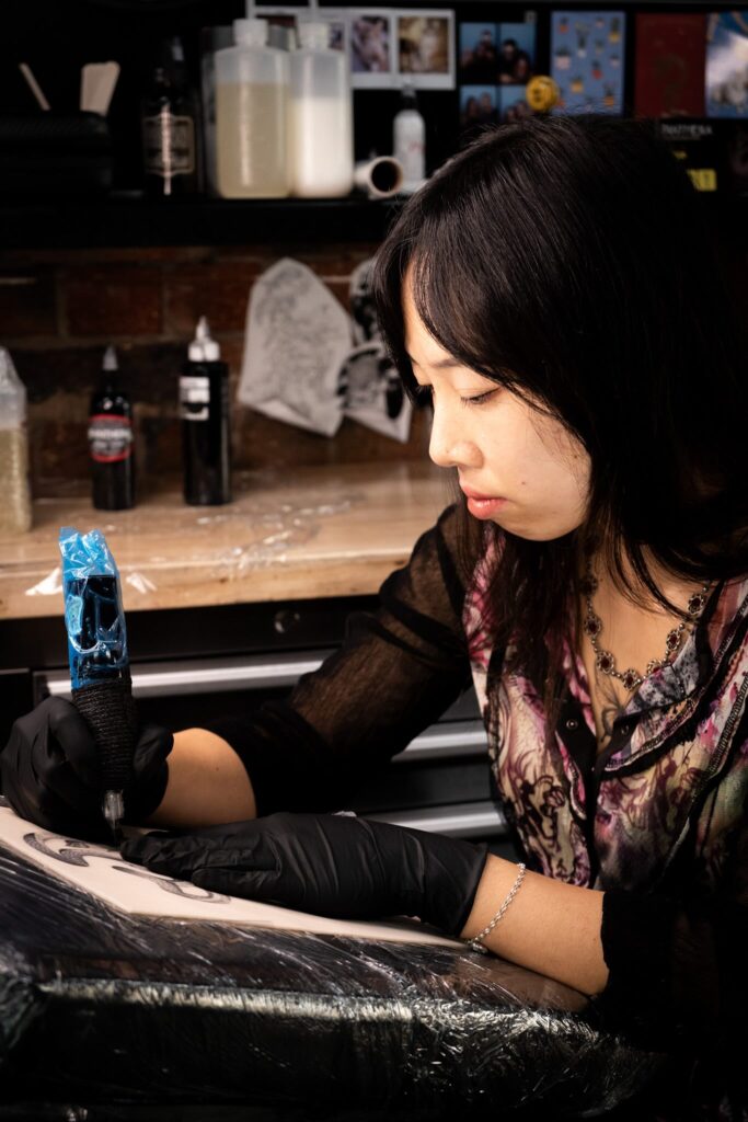 Tattoo artist working intently with tattoo machine on armrest; supplies in the background.