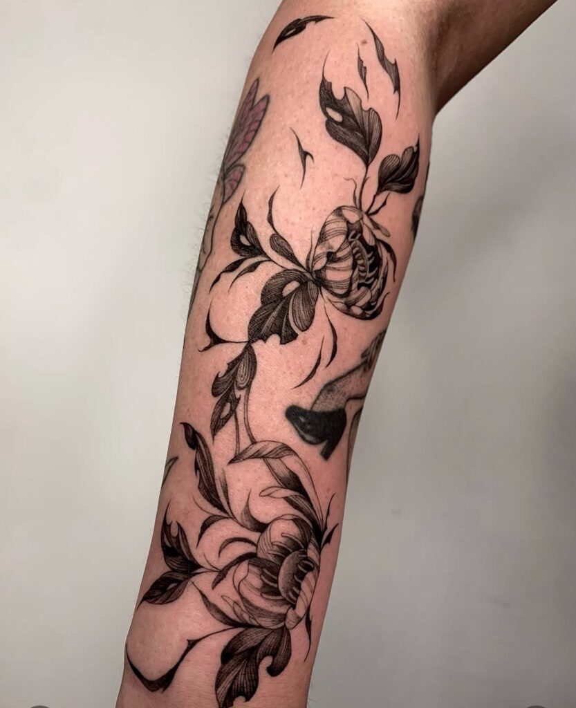 Black ink floral tattoo with detailed leaves and petals on a forearm.