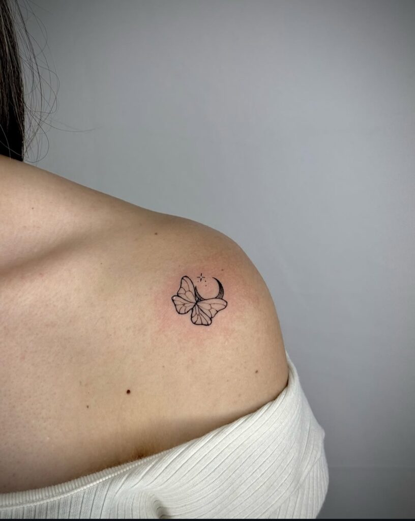 Small tattoo of a butterfly with crescent moon and stars on upper shoulder of a person in white top