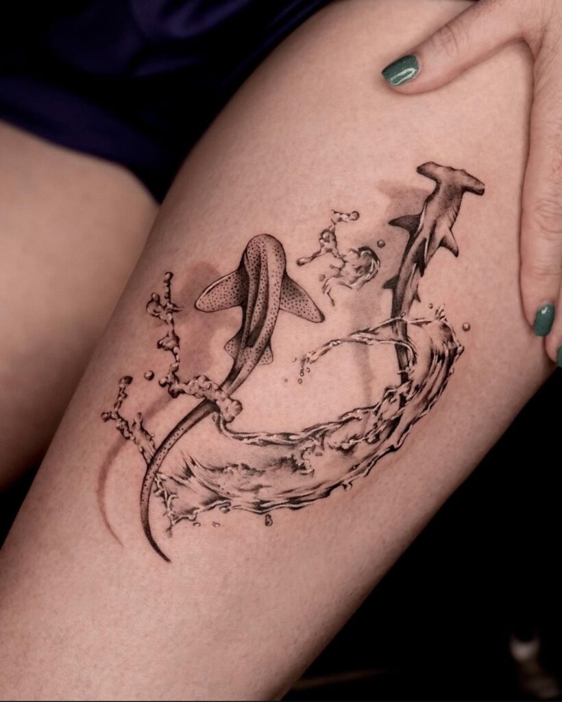 Tattoo of two hammerhead sharks swimming in a circle with splashing water on a thigh.