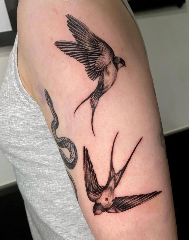 Black and grey tattoo of two flying swallows on the upper arm