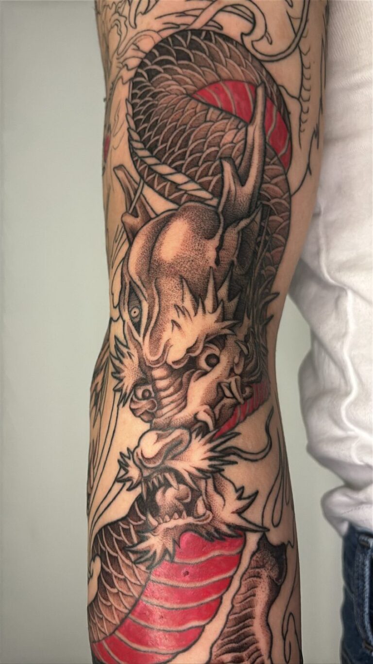 Detailed dragon fantasy tattoo with red accents on arm