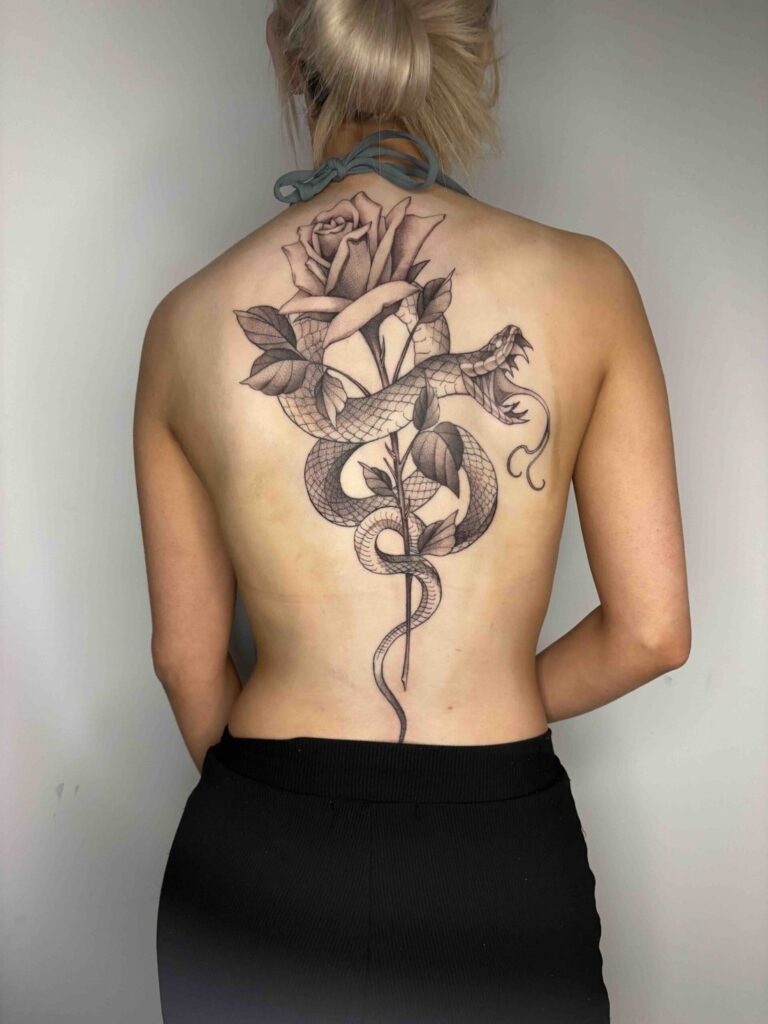 Monochromatic tattoo of a rose and snake intertwined on a person's back.