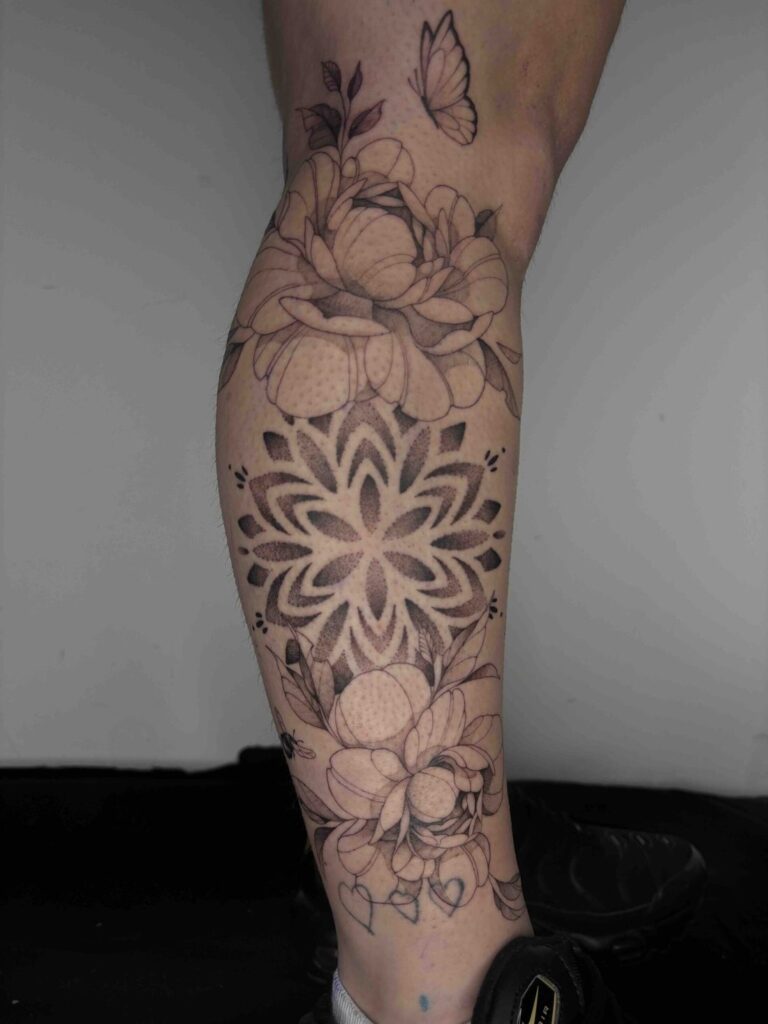 Leg tattoo with intricate floral design, butterfly above, detailed shading, and geometric patterns.