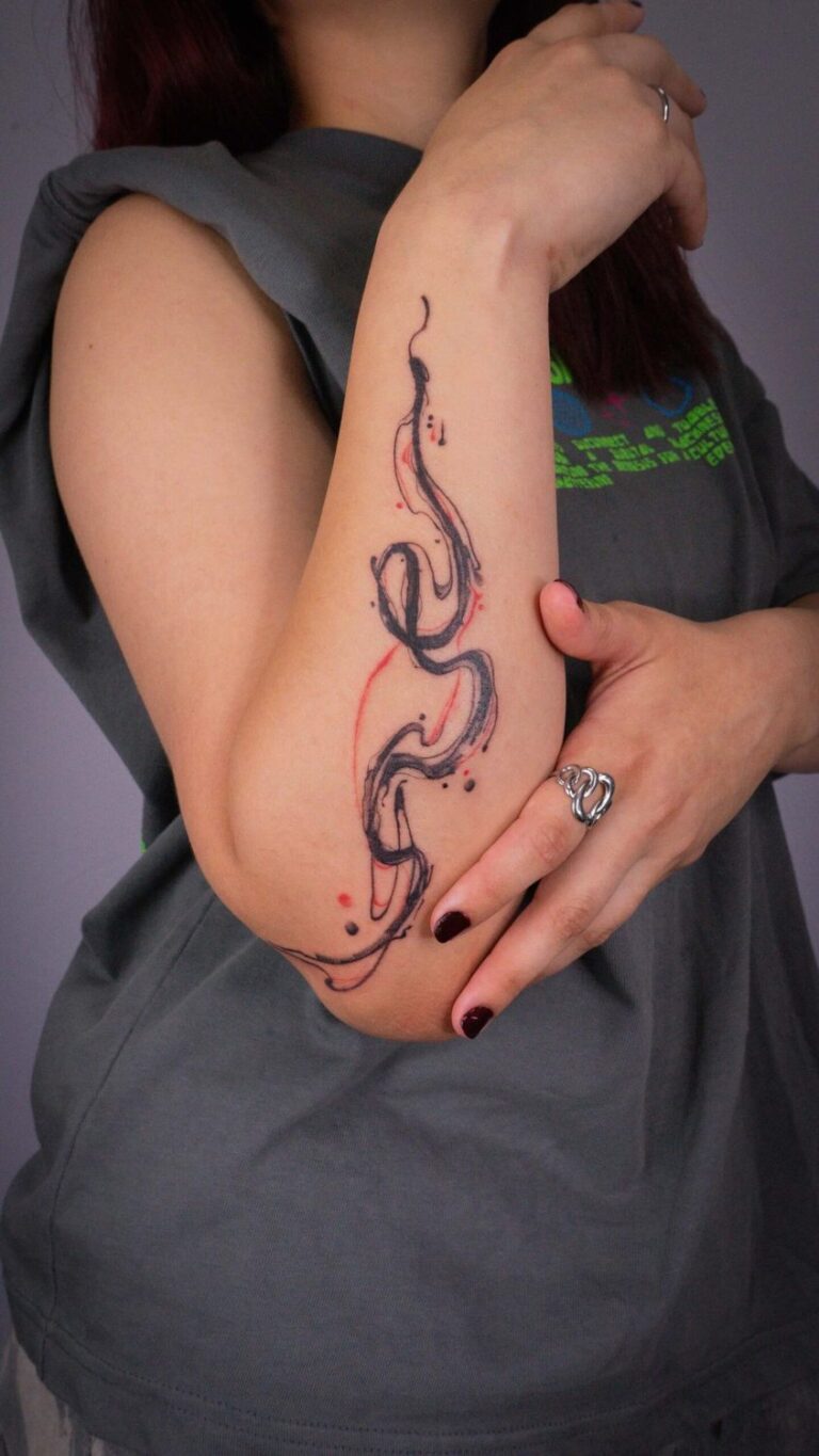 Person with long hair showing forearm tattoo of a black line with red accents, grey shirt.