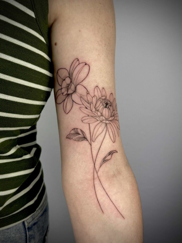 Tattoo of two flowers and leaves on upper arm, person in green and white striped top.