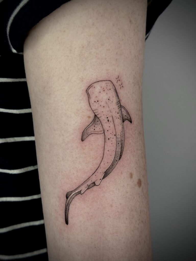 Minimalist whale shark tattoo on upper arm with fine lines and dot-detail pattern.