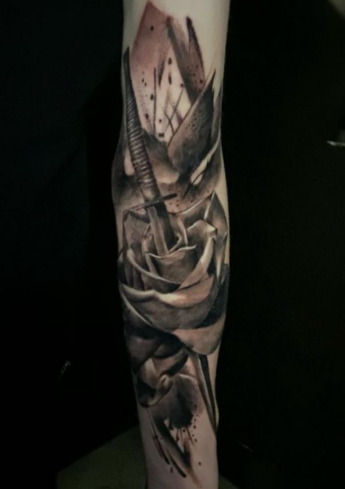 Forearm tattoo of a rose and sword in black and grey with abstract splatters and shapes.