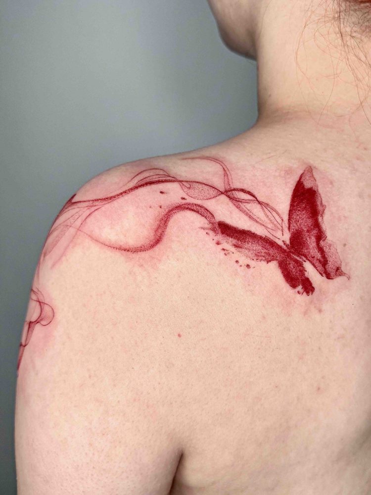 Red butterfly tattoo with flowing wisps across the shoulder blade by Woody