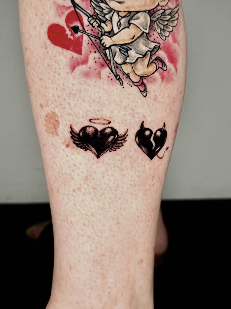 Pair of small black heart tattoos beneath an existing coloured design by Woody