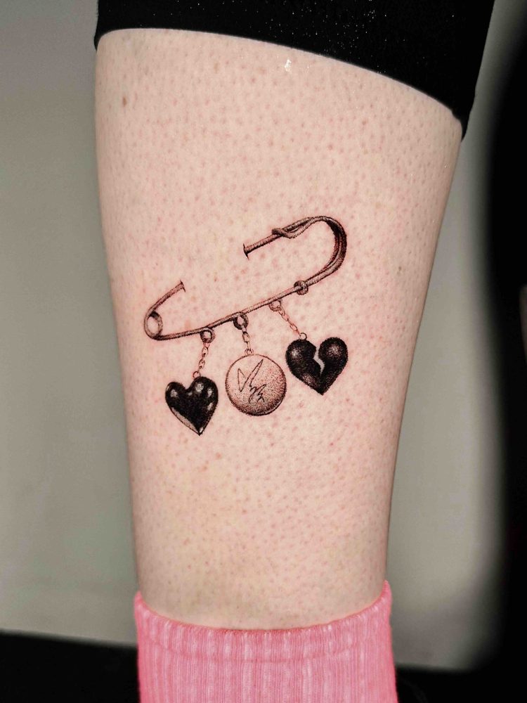 Safety pin tattoo with hanging heart and round charms by Woody