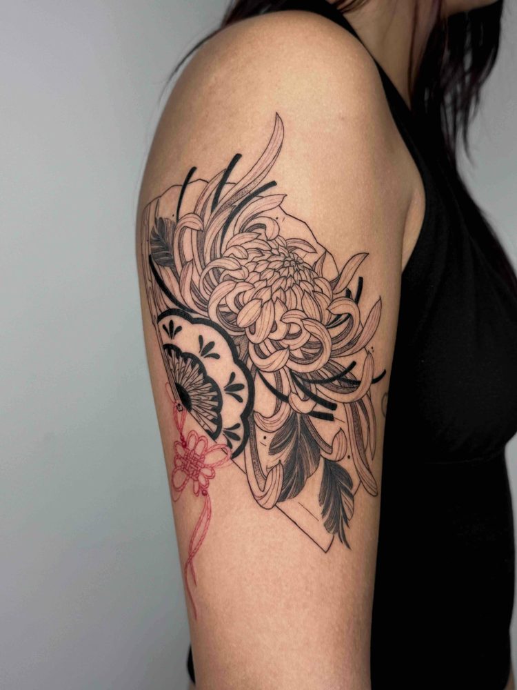 Intricate black and red tattoo with chrysanthemum and fan design on upper arm.