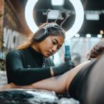 Photo of female tattoo artist with headphones tattooing client's arm