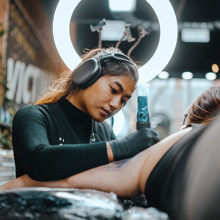 Photo of female tattoo artist with headphones tattooing client's arm