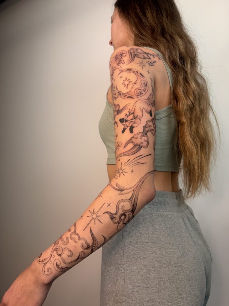 Side view of a black and grey sleeve with celestial motifs and ornamental lines from shoulder to wrist by Chanelle Pititto.
