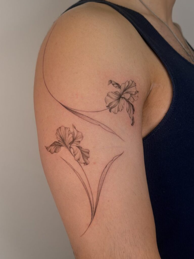 Two fine line flowers with long curved stems on the upper arm by Chanelle Pititto.