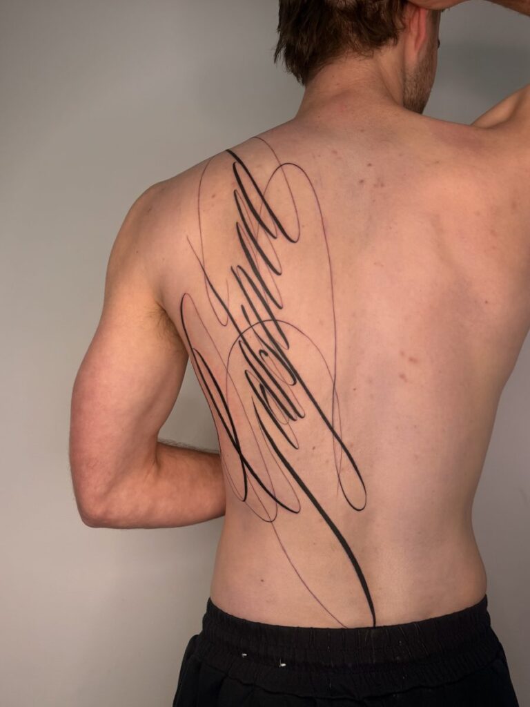 Large flowing script tattoo with sweeping flourishes across the upper back by Chanelle Pititto.