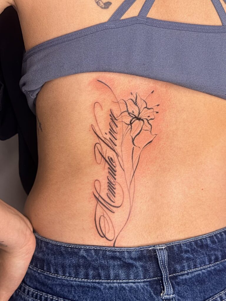 Flowing script beside a fine line flower on the side of the torso by Chanelle Pititto.